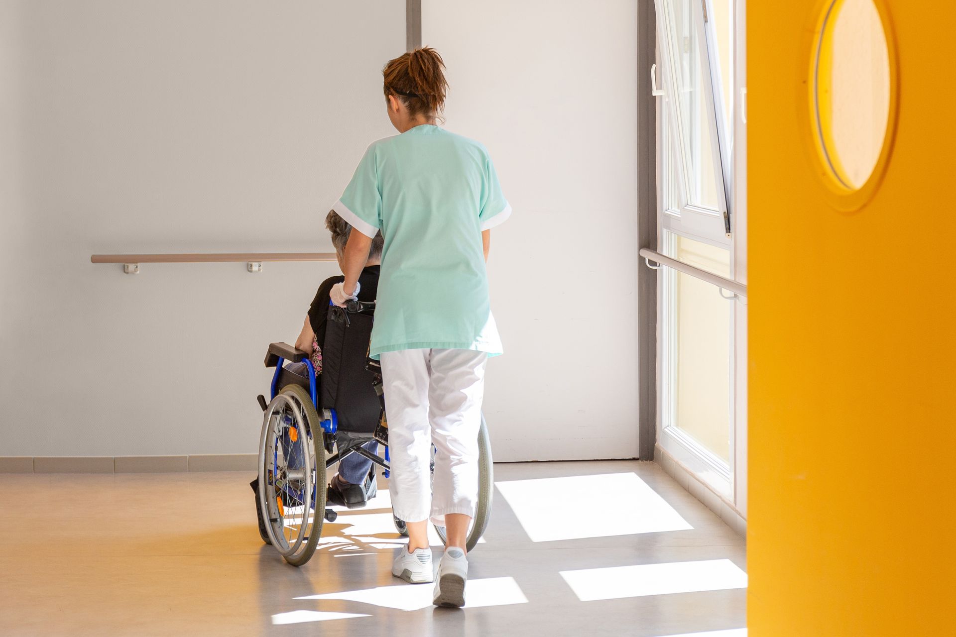 Eine Krankenschwester schiebt einen Patienten im Rollstuhl einen Flur entlang.