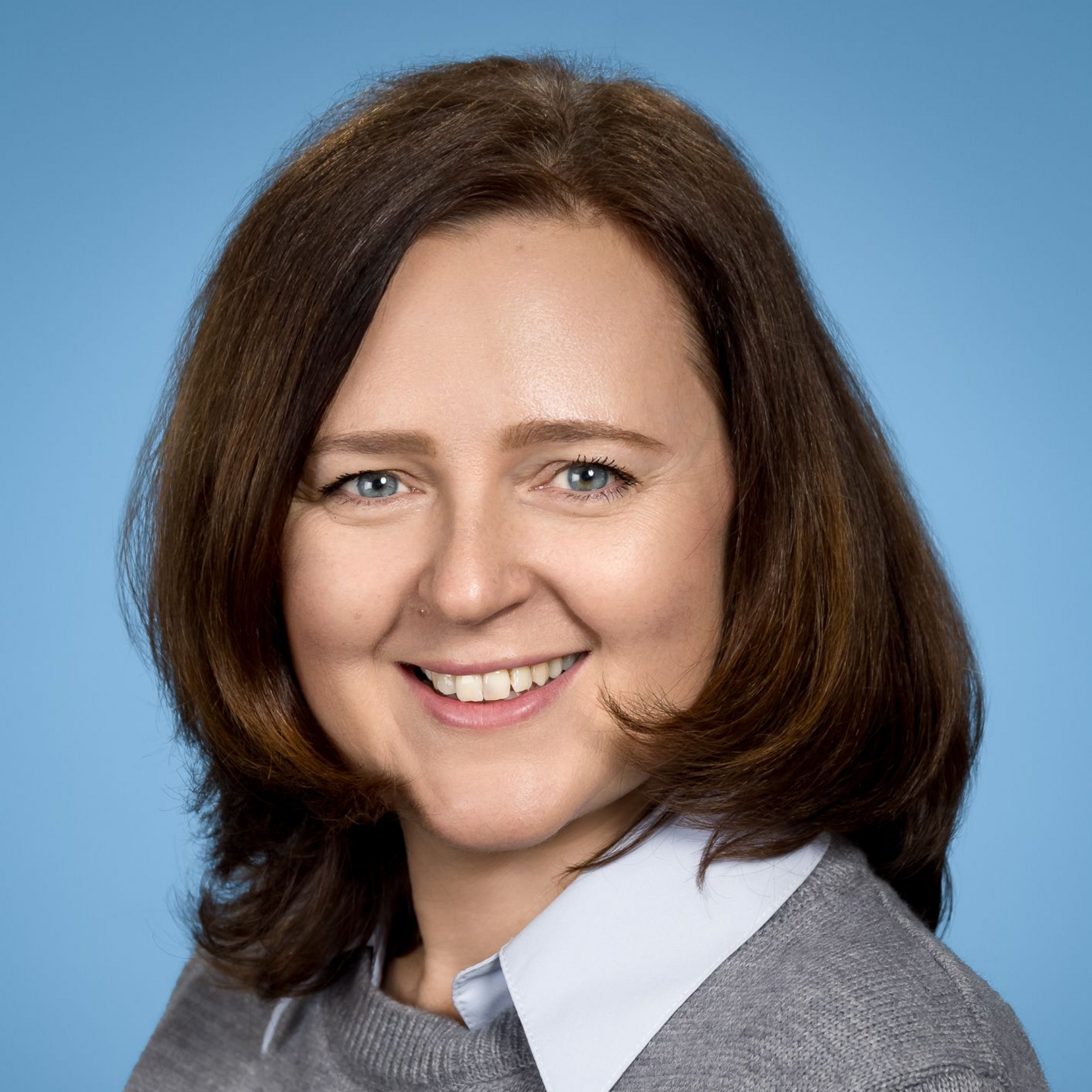 Eine Frau mit Brille und weißem Hemd lächelt in die Kamera.