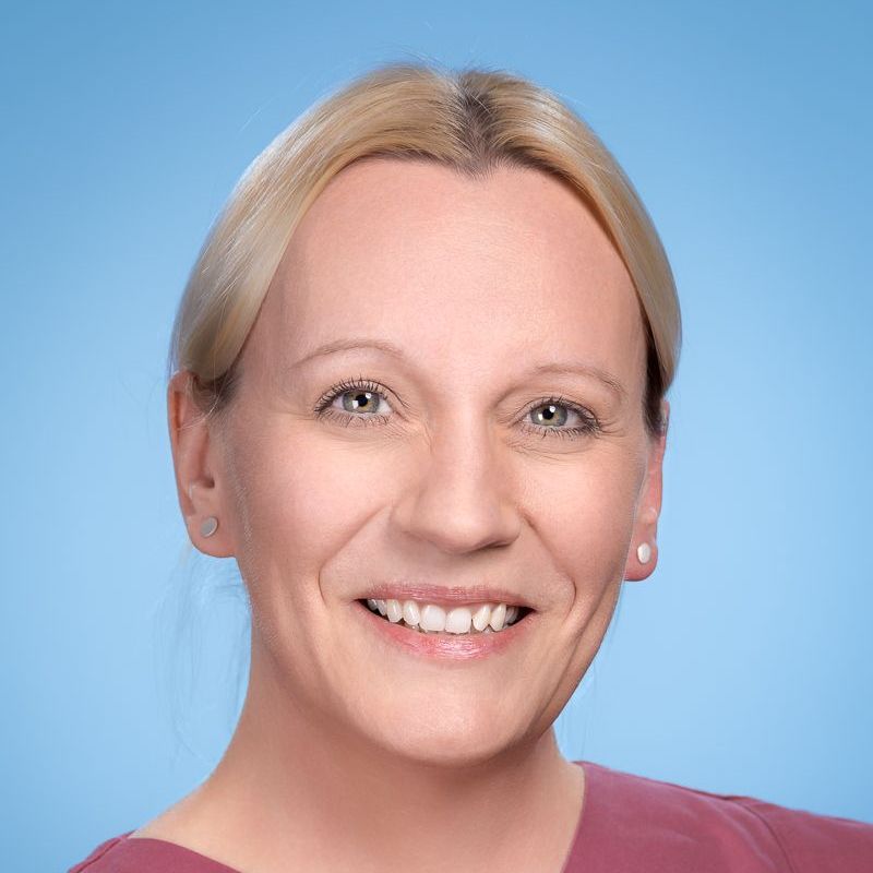 Eine Nahaufnahme des lächelnden Frauengesichts vor blauem Hintergrund.
