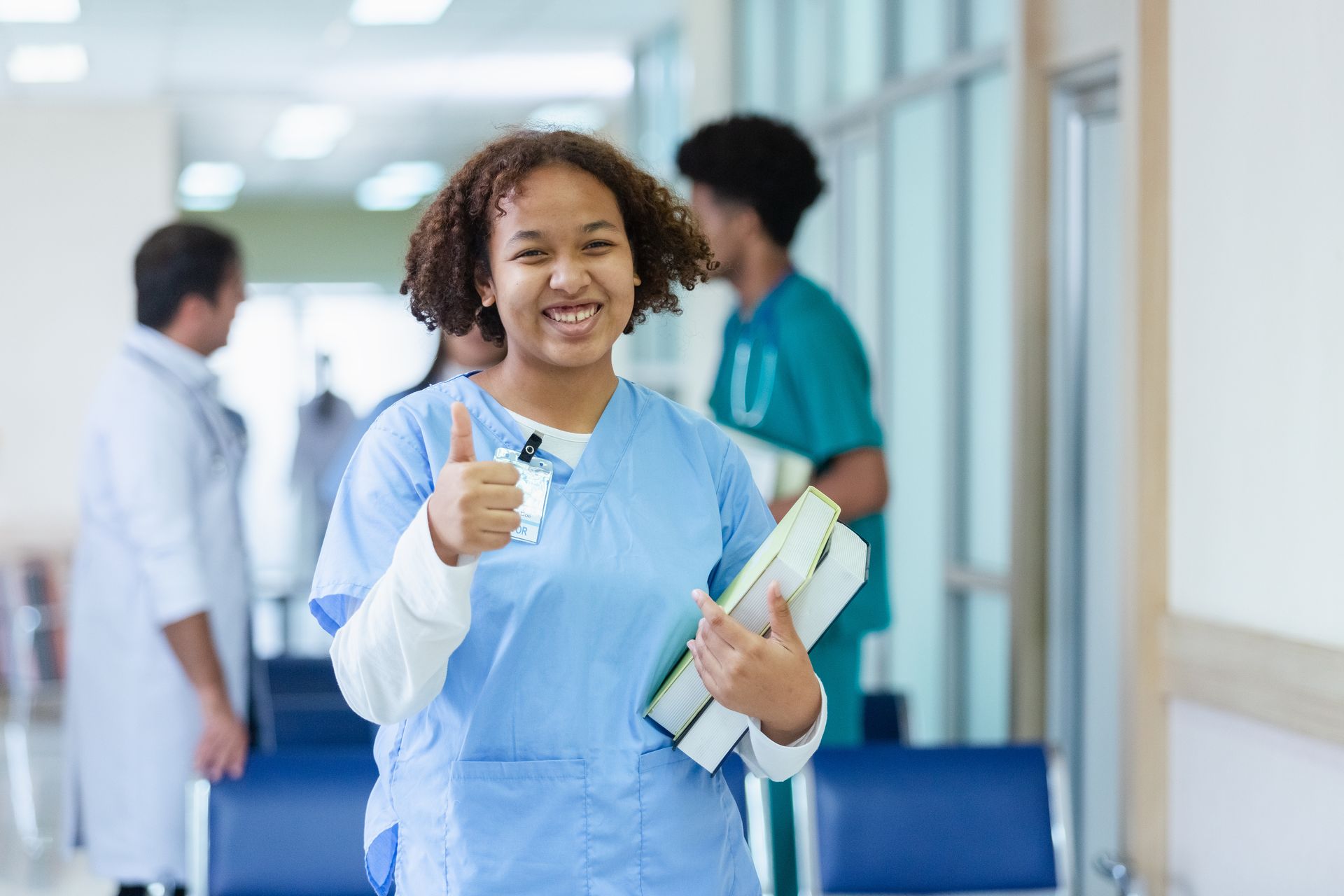Eine Krankenschwester zeigt im Flur eines Krankenhauses den Daumen nach oben.