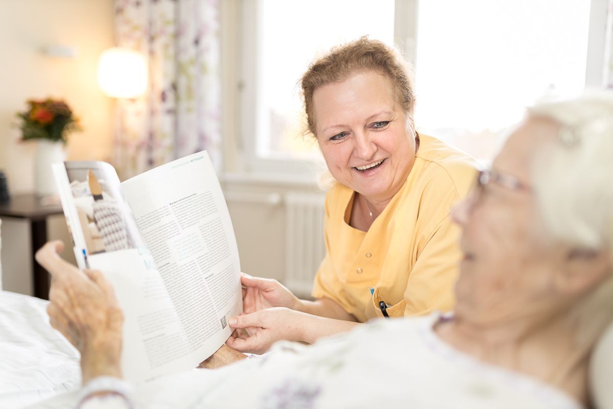 Eine Krankenschwester liest einer älteren Frau im Krankenhausbett ein Buch vor.