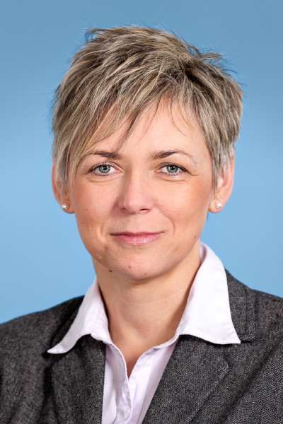 Eine Frau in Anzug und weißem Hemd lächelt in die Kamera.
