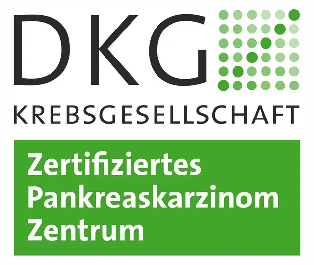 Ein kahlköpfiger Mann in weißem Kittel und Krawatte lächelt in die Kamera.
