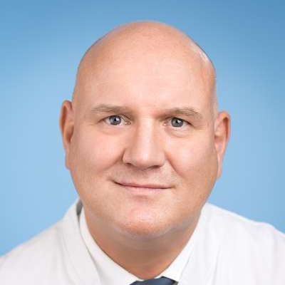 Ein kahlköpfiger Mann in weißem Hemd und Krawatte lächelt in die Kamera.