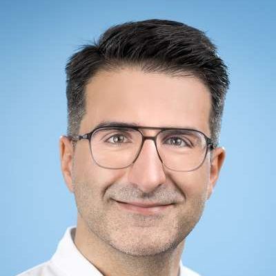 Ein Mann mit Brille und weißem Hemd lächelt in die Kamera.