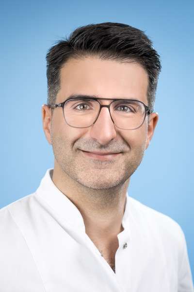 Ein Mann mit Brille und weißem Kittel lächelt in die Kamera.