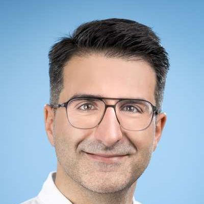 Ein Mann mit Brille und weißem Hemd lächelt in die Kamera.