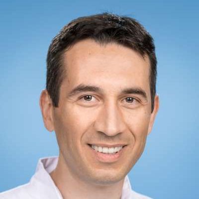 Vor einem blauen Hintergrund lächelt ein Mann in die Kamera.