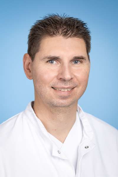 Ein Mann im weißen Laborkittel lächelt in die Kamera.