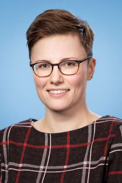 Eine Frau mit Brille und kariertem Hemd lächelt in die Kamera