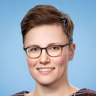 Eine Frau mit Brille und kariertem Hemd lächelt in die Kamera.