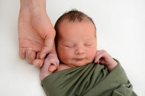 Ein Mann hält ein neugeborenes Baby, das in eine grüne Decke gewickelt ist.