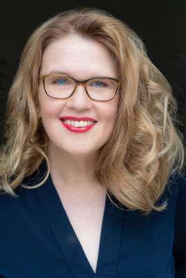Eine Frau mit Brille und blauer Jacke lächelt in die Kamera.