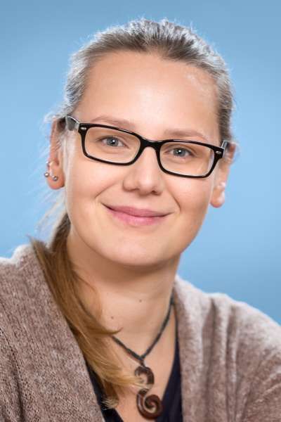 Eine Frau mit Brille und Halskette lächelt in die Kamera.