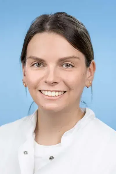 Eine Frau in einem weißen Laborkittel lächelt in die Kamera.