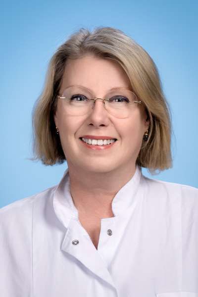 Eine Frau mit Brille und weißem Laborkittel lächelt in die Kamera.
