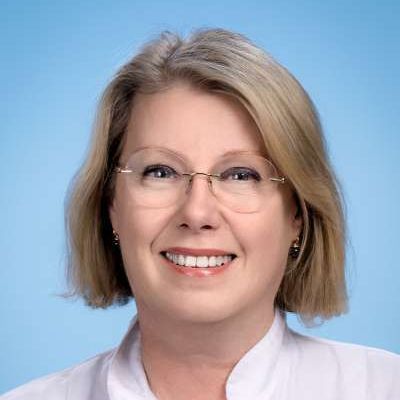 Eine Frau mit Brille und weißem Hemd lächelt in die Kamera.