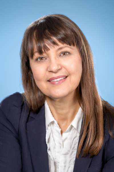 Eine Frau in einer blauen Jacke und einem weißen Hemd lächelt in die Kamera.