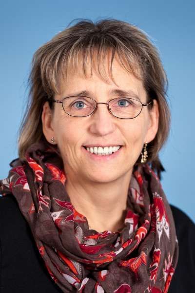 Eine Frau mit Brille und Schal lächelt in die Kamera.