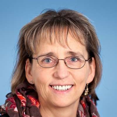 Eine Frau mit Brille und Schal lächelt in die Kamera.