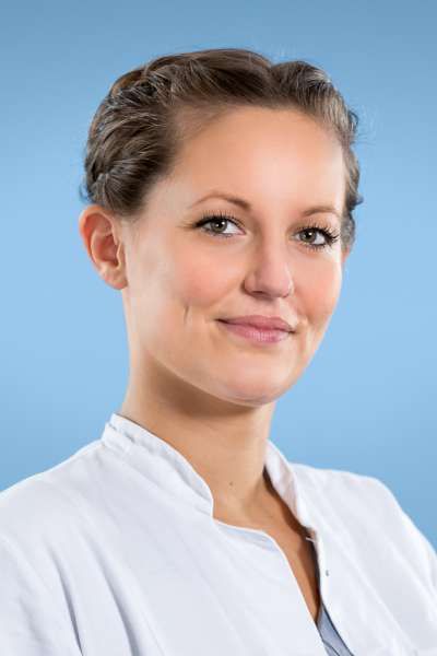Eine Frau in einem weißen Laborkittel lächelt in die Kamera.