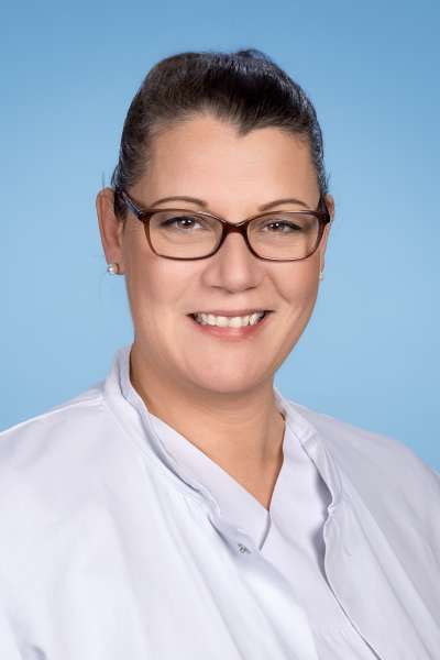Eine Frau mit Brille und weißem Hemd lächelt in die Kamera.