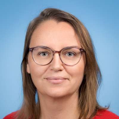 Eine Frau mit Brille und rotem Hemd lächelt in die Kamera.