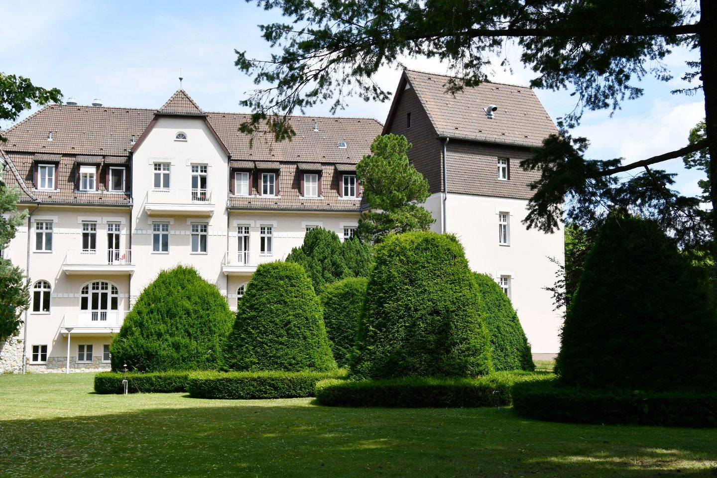 Ein großes weißes Gebäude ist von Bäumen und Büschen umgeben