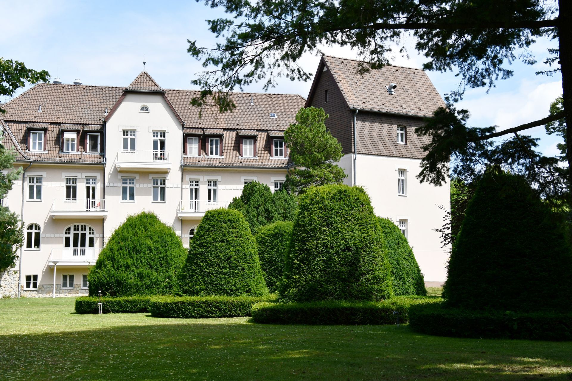 Ein großes weißes Gebäude ist von Bäumen und Büschen umgeben