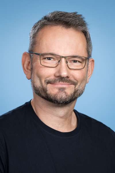 Ein Mann mit Bart und Brille lächelt in die Kamera.