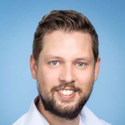 Ein Mann mit Bart und einem weißen Hemd lächelt in die Kamera.