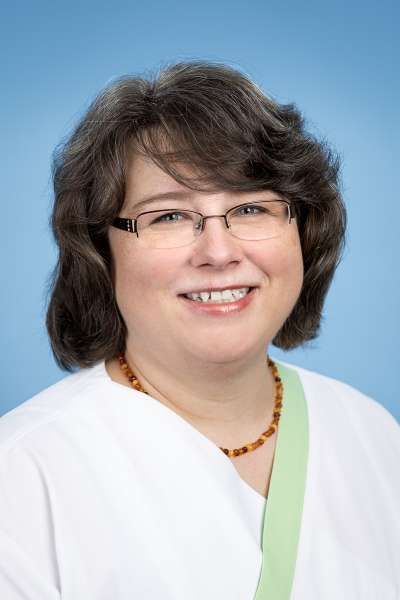 Eine Frau mit Brille und Schal lächelt in die Kamera.