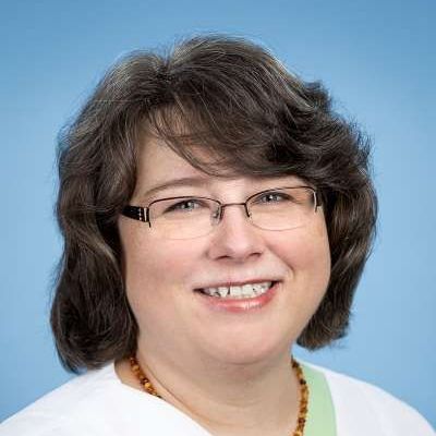 Eine Frau mit Brille und Halskette lächelt in die Kamera.