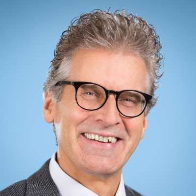 Ein Mann mit Brille und Anzug lächelt in die Kamera.