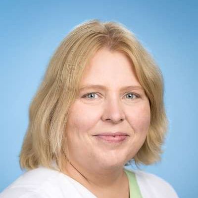 Eine Frau mit blonden Haaren und grünen Augen lächelt in die Kamera.