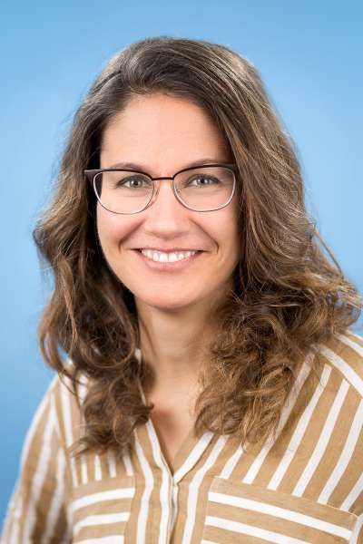 Eine Frau mit Brille und gestreiftem Hemd lächelt in die Kamera.