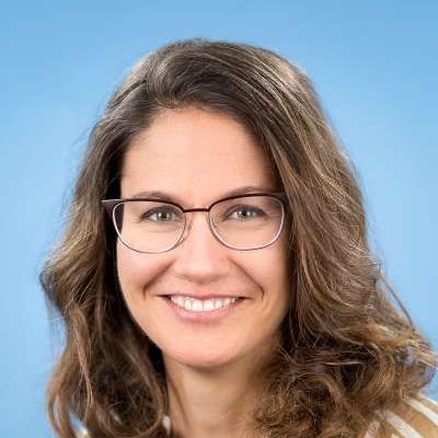 Eine Frau mit Brille und gestreiftem Hemd lächelt in die Kamera.