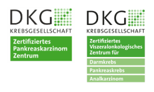 Ein kahlköpfiger Mann in weißem Kittel und Krawatte lächelt in die Kamera.