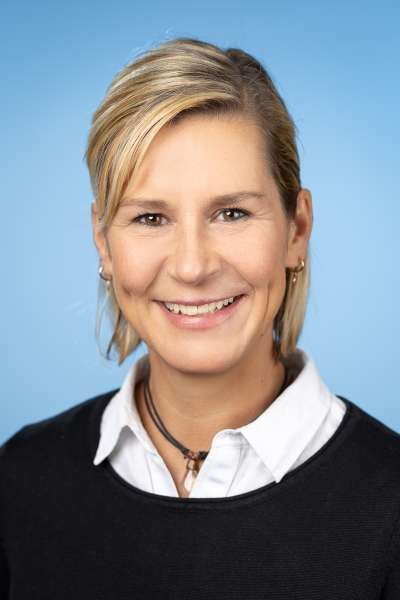 Eine Frau in einem schwarzen Pullover und einem weißen Hemd lächelt in die Kamera.