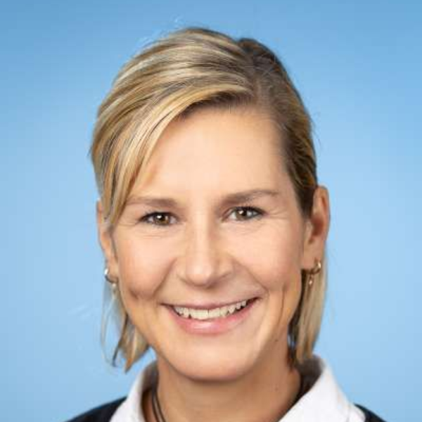 Eine Frau in einem schwarzen Pullover und einem weißen Hemd lächelt in die Kamera.
