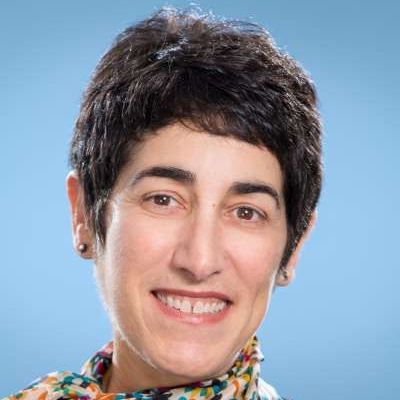 Eine Frau mit kurzen Haaren lächelt und trägt einen bunten Schal.