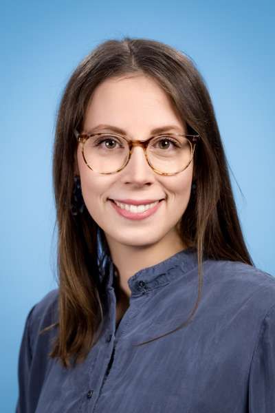 Eine Frau mit Brille und blauem Hemd lächelt in die Kamera.
