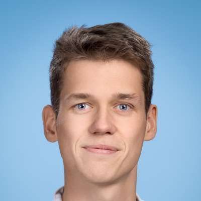 Ein junger Mann lächelt vor einem blauen Hintergrund in die Kamera.