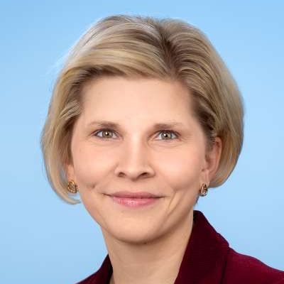 Eine Frau in einer roten Jacke und mit Ohrringen lächelt in die Kamera.