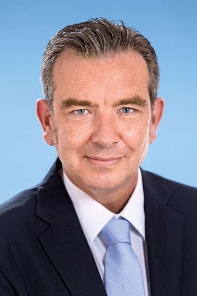 Ein Mann in Anzug und Krawatte lächelt in die Kamera.