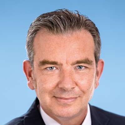 Ein Mann in Anzug und Krawatte lächelt in die Kamera.