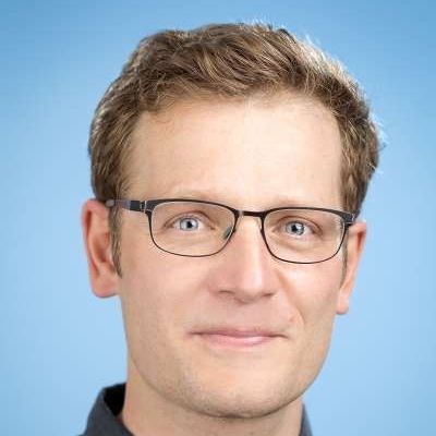 Ein Mann mit Brille und schwarzem Hemd lächelt in die Kamera.