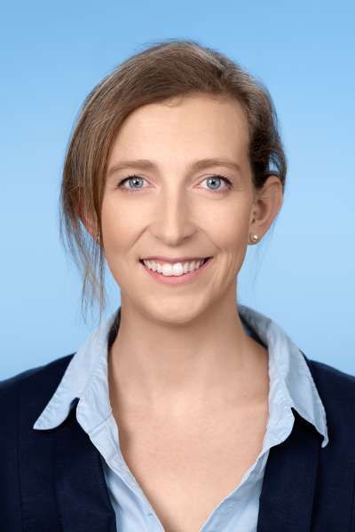 Eine Frau in Anzug und blauem Hemd lächelt in die Kamera.