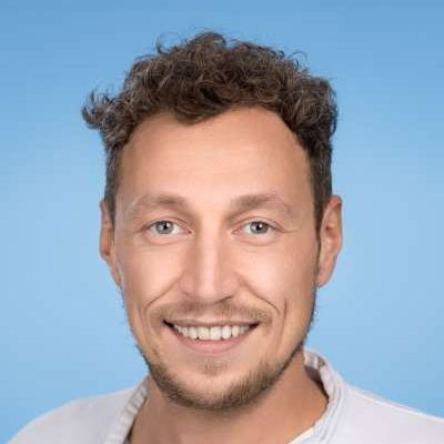 Ein Mann mit lockigem Haar und Bart lächelt in die Kamera.