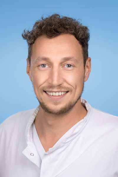 Ein Mann im weißen Laborkittel lächelt in die Kamera.